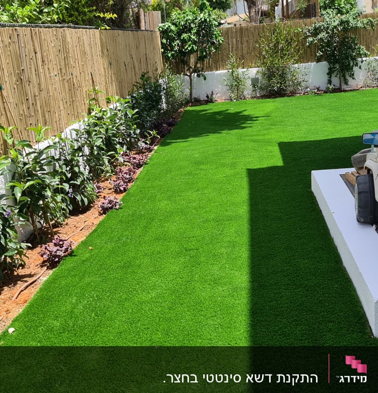 שיחים ירוקים לאורך גדר במרפסת עם דשא סינתטי